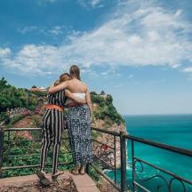 two women standing on a ledge looking at the ocean
