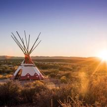a red and white teepee in the desert with the sunset