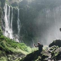 two people standing on rocks near a waterfall