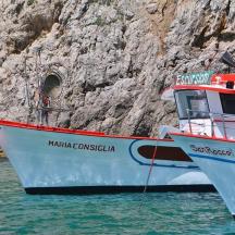 two boats sitting in the water next to a cliff