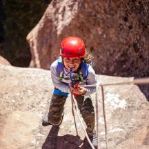 a young girl in a red helmet climbing on a rock