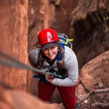 a woman in a red helmet is climbing a cliff