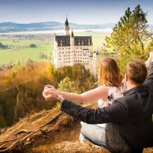 a man and a woman sitting on a rock in front of a castle