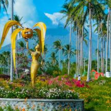 a gold statue in a garden with palm trees