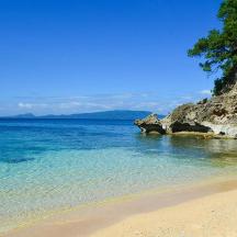 a beach with clear blue water and a cliff