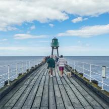 a group of people walking on a pier with a lighthouse