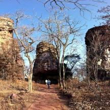 a person walking down a dirt road next to two large rocks