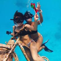two women in bathing suits sitting on a bike in the water
