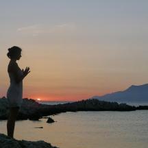 una dona dempeus a la platja a la posta de sol