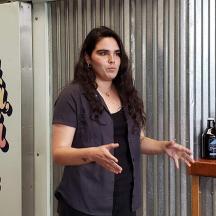 Una mujer parada junto a un mostrador con botellas de vino.