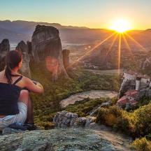 a woman sitting on top of a mountain watching the sunset