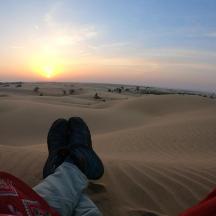 una persona asseguda al desert mirant la posta de sol