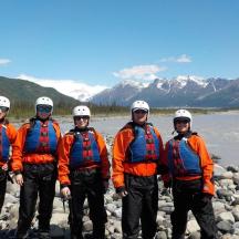 eine Gruppe von Männern in orangefarbenen Jacken steht neben einem Fluss