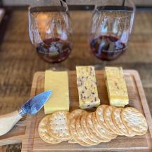 a cutting board with cheese and two glasses of wine