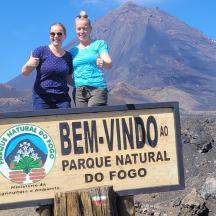 two people standing on top of a sign in front of a mountain