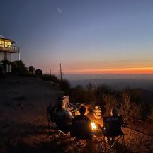 a group of people sitting in chairs on a hill at sunset
