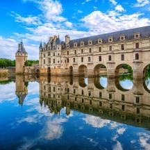 a castle reflecting in the water in front of a bridge