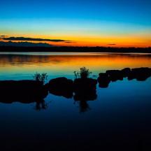 a sunset over a lake with rocks in the water