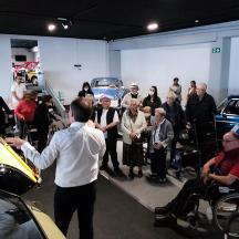 eine Gruppe von Menschen in einer Garage, die sich Autos anschauen