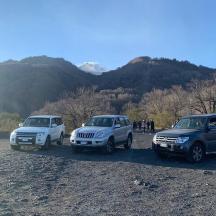 three vehicles parked next to a river with mountains in the background
