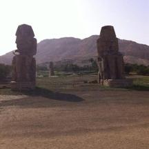 two stone statues in a field with mountains in the background