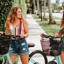 two young women riding bikes down a sidewalk