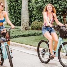 two young women riding bikes down a street