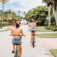 two women riding bikes down a street with palm trees