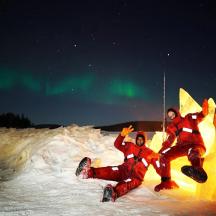 two people are standing in the snow under the northern lights
