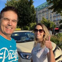 a man and woman giving a thumbs up in front of a taxi