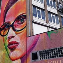 ein großes Wandbild einer Frau mit Brille an einem Gebäude