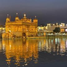 a lit up golden temple in front of the water at night