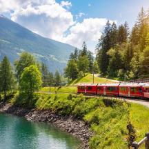 ein roter Zug, der die Gleise neben einem Fluss entlangfährt