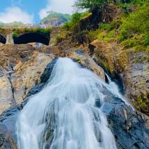 ein Wasserfall auf einer Klippe mit einer Brücke im Hintergrund