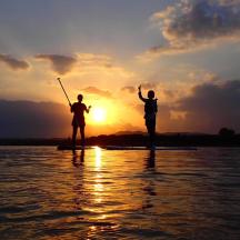 two people are standing in the water at sunset