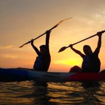 two people in a kayak on the water at sunset