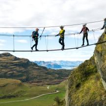 a group of people walking on a rope bridge on a mountain