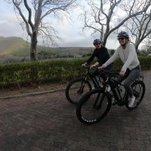 two people riding bikes down a brick road