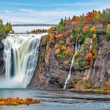a waterfall on a cliff with a bridge in the background