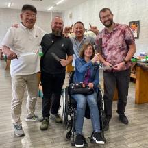eine Gruppe von Männern steht um eine Frau im Rollstuhl herum