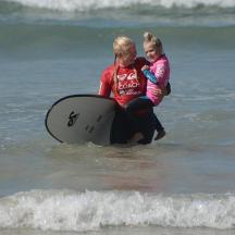 a woman and a child sitting on a surfboard in the ocean