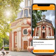 eine Person, die vor einem Gebäude ein Mobiltelefon hochhält
