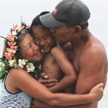 a woman and two men hugging a young child