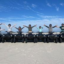 a group of people standing on four four wheelers in the sand