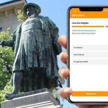 asmuo, laikantis mobilųjį telefoną priešais statulą