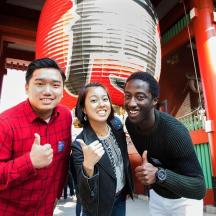 two men and a woman giving thumbs up in front of a building