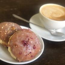 two donuts on a plate next to a cup of coffee