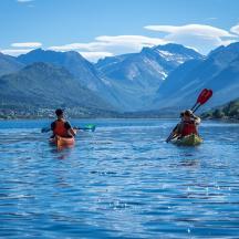 two people kayaking on a lake with mountains in the background