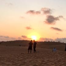 a group of people standing on a beach at sunset