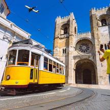 a woman taking a picture of a yellow tram in front of a church